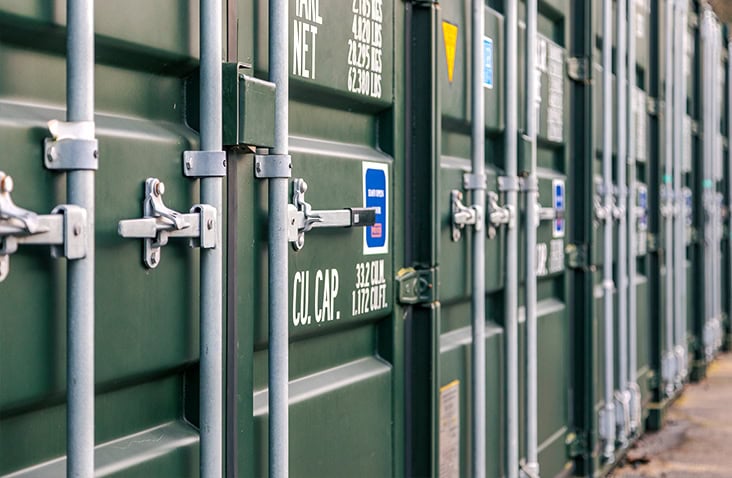     Row of green shipping container doors and locking bars, highlighting hardware and door mechanisms. 