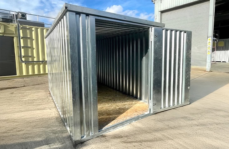 Interior view of a galvanised 2m x 3m flat pack storage unit with open door, showing ribbed steel walls and timber flooring. 