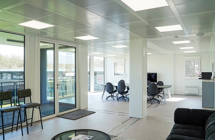 Light-filled modular interior combining office seating, lounge furniture, and access to an external balcony.
