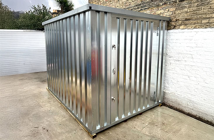 Galvanised 2m x 3m flat pack storage unit installed in a small outdoor courtyard space next to a brick wall. 