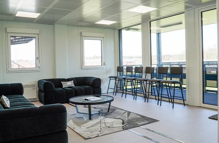 Open-plan modular lounge with sofas, a coffee table, bar seating, and large windows overlooking the surroundings.