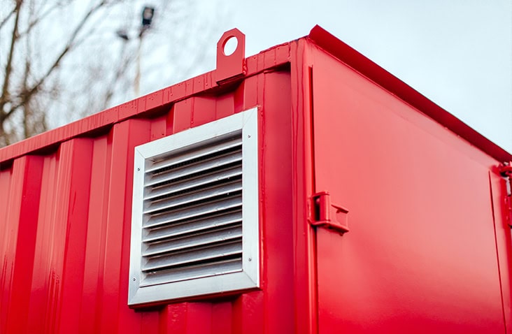     Close-up of a red shipping container fitted with a metal ventilation grille on the side panel. 