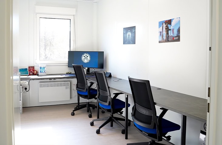 Modern modular office with three workstations, ergonomic chairs, and a large window providing natural light.