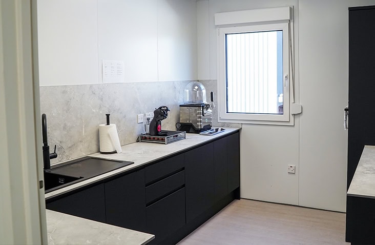 Modern modular kitchen installation featuring black cabinetry, integrated appliances, and a marble-effect countertop.