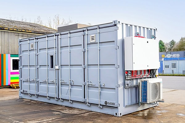 A converted grey shipping container fitted with ventilation, blast panels, and external electrical equipment, designed as a battery storage unit.