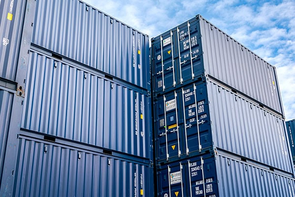 Large stepped stack of blue S Jones Containers on an industrial site under a clear sky.