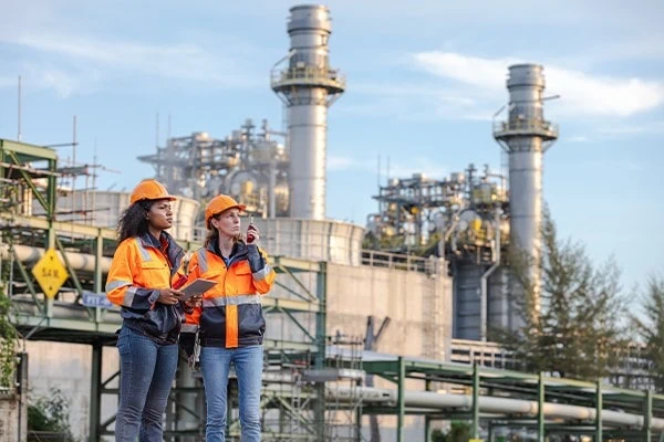 Two industrial engineers in high-visibility clothing are reviewing plans at an industrial processing plant, representing infrastructure, manufacturing and engineering operations. 