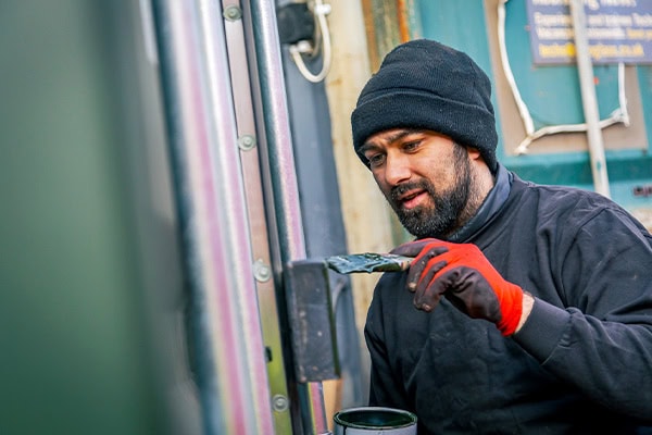 A member of staff painting a shipping container component by hand during container repair and maintenance work.