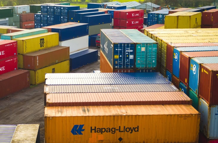 Aerial view of a large shipping container depot with rows of stacked containers in multiple colours, showing organised container storage and logistics yard operations.