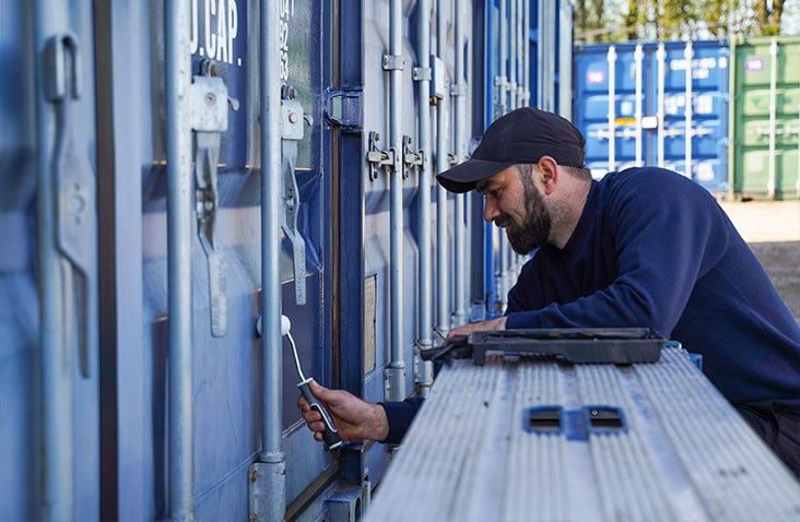 A technician using a brush to apply ClearRestore® treatment to the locking gear of a blue shipping container.