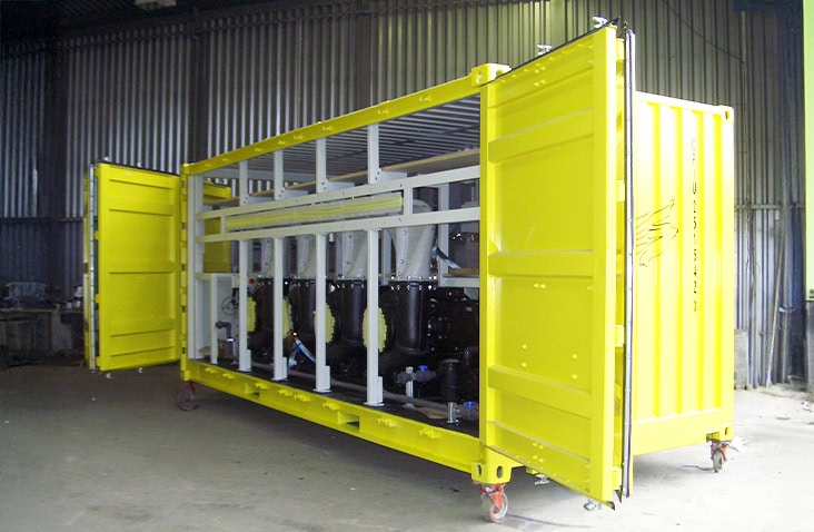 Side-opening 20ft shipping container conversion housing industrial water pumps and pipework, painted yellow and shown with full-width doors open inside a workshop environment. 