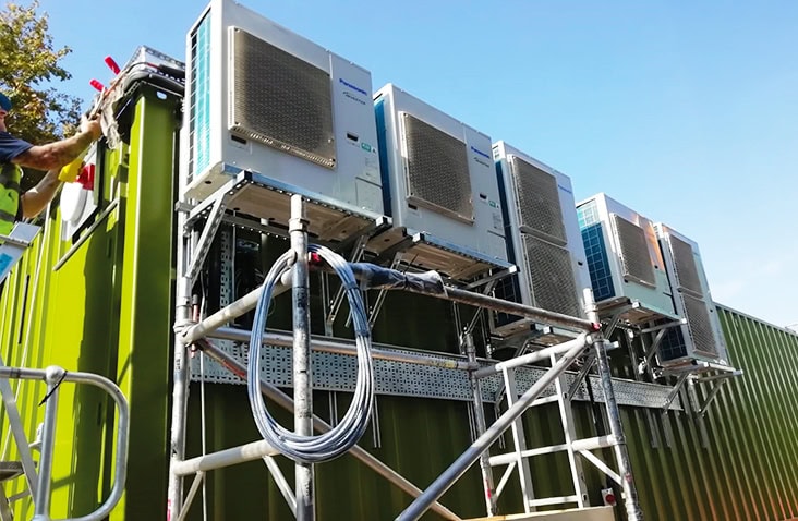External HVAC units installed on a containerised switchgear enclosure, showing multiple wall-mounted air conditioning systems on a green converted shipping container to provide cooling for electrical equipment. 