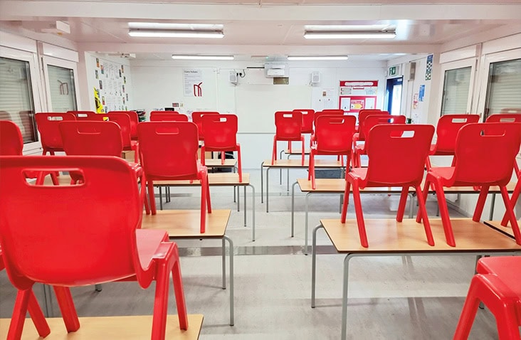 Interior of a modular classroom within a modular school building, showing student desks with chairs, bright lighting, teaching displays and a clean, modern learning environment.