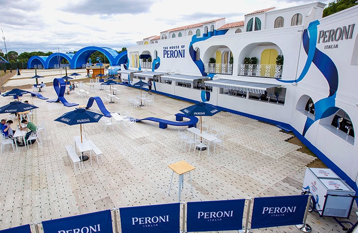 Wide view of The House of Peroni containerised event venue, featuring white shipping containers with blue Peroni branding, outdoor seating, branded umbrellas and bar areas arranged across a paved hospitality space.
