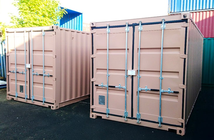 Two 20ft shipping containers with bespoke external modifications, shown closed and finished in matching paintwork, positioned in a container yard ready for deployment.