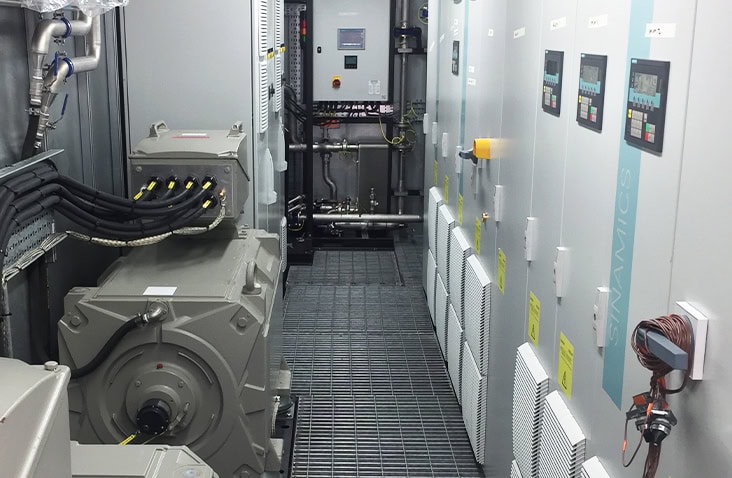 Interior of a converted shipping container housing industrial electrical control panels, motors and pipework, showing a fully integrated plant room with grated flooring, cable management and engineered systems installation.