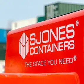 Close-up of red container handling equipment branded with the S Jones Containers logo and the slogan “The space you need,” with stacked shipping containers visible in the background at their West Midlands container depot.