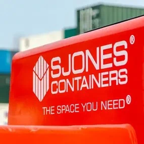 Close-up of red container handling equipment branded with the S Jones Containers logo and the slogan “The space you need,” with stacked shipping containers visible in the background at their West Midlands container depot.