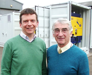 Two men standing at an S Jones Containers site in front of an open white shipping container housing industrial equipment, representing early container engineering and conversion work in the company’s history. 