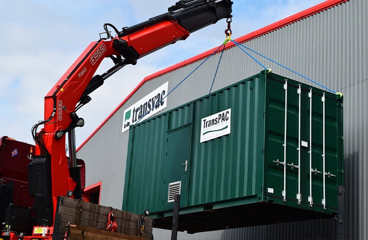 20ft shipping container housing a PAC dosing system for water treatment being crane lifted, showing a green TransPAC container with personnel door and vented panels during delivery and installation at an industrial site.