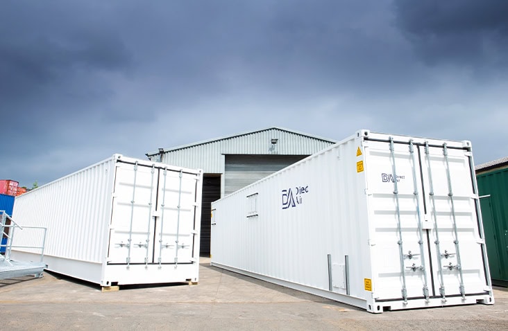 20ft control room container and 40ft compressor enclosure on site, showing white converted shipping containers with secure cargo doors, ventilation features and Direct Air branding positioned outside an industrial facility. 