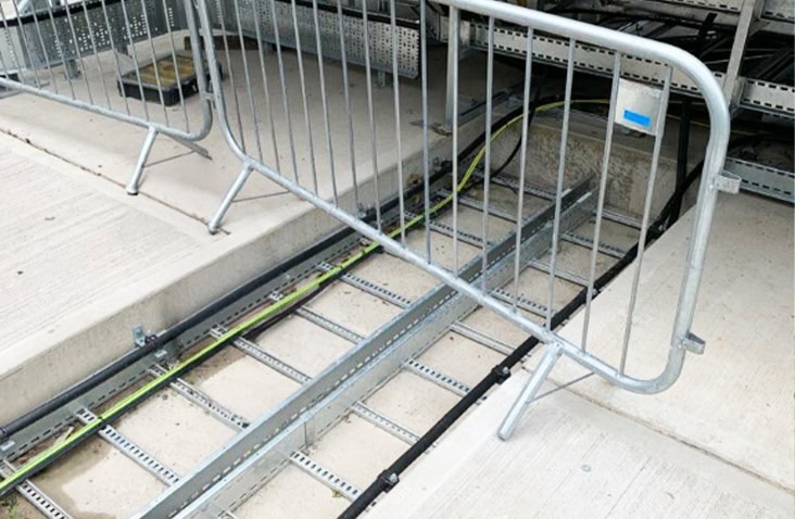 Electrical cable containment and routing outside a container, showing power and data cables installed in galvanised cable trays with temporary safety barriers at a containerised electrical installation. 