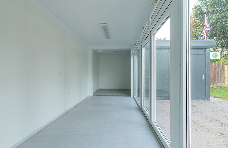Internal corridor view inside a modular building, showing a clean, modern interior with integrated lighting, smooth wall finishes and glazed external doors providing access to outdoor space.
