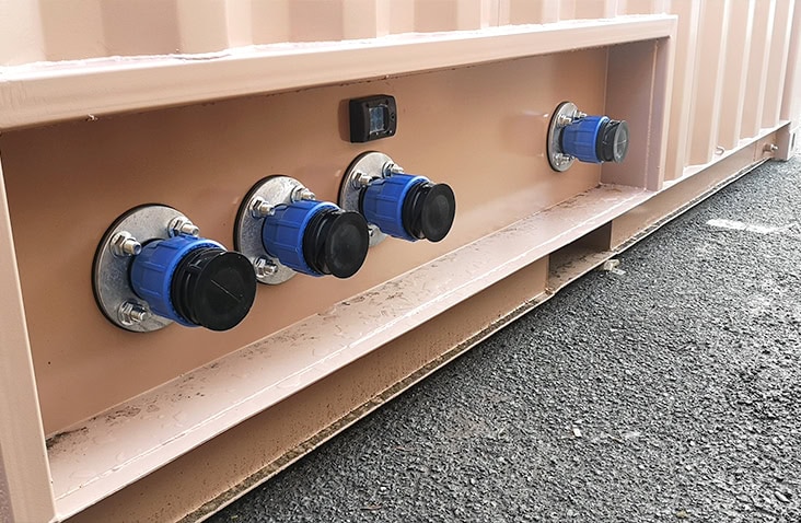 Close-up of exterior pipe connections on a water treatment container, showing multiple blue industrial fittings mounted through the container wall for fluid inlet and outlet connections.