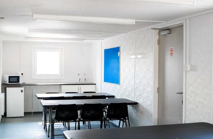     Interior of a fitted site canteen hire unit showing dining tables, chairs, kitchenette with sink and microwave, notice boards and lighting, providing clean and comfortable welfare facilities for site staff. 