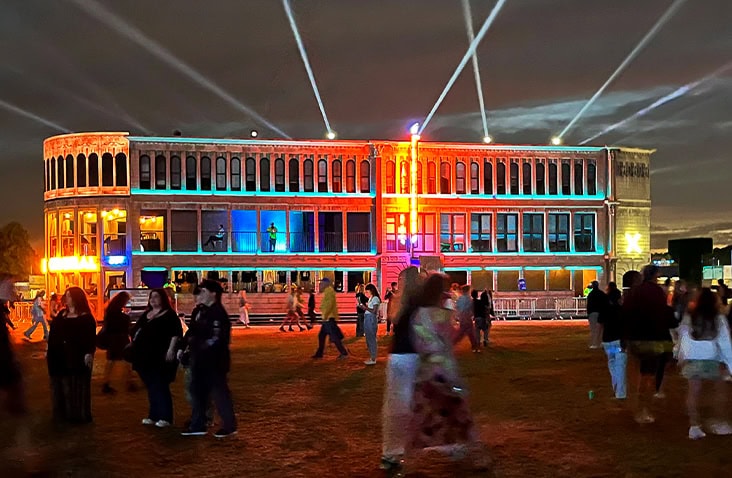 Completed containerised Flatiron building illuminated at night, showcasing a large-scale shipping container conversion used as an event venue with architectural lighting and crowd access.
