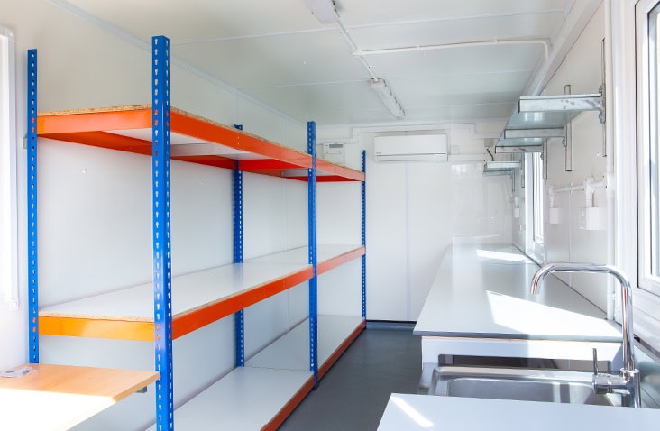 Interior of a containerised laboratory conversion, showing clean white wall panels, integrated worktops, shelving, lighting and temperature-controlled environment inside a modified shipping container. 