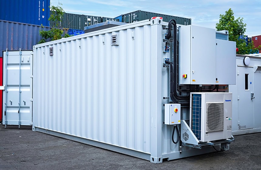 Battery storage container with integrated blast panel and HVAC system, showing a white converted shipping container fitted with external electrical cabinets, ventilation, cooling equipment and safety features for energy storage applications.
