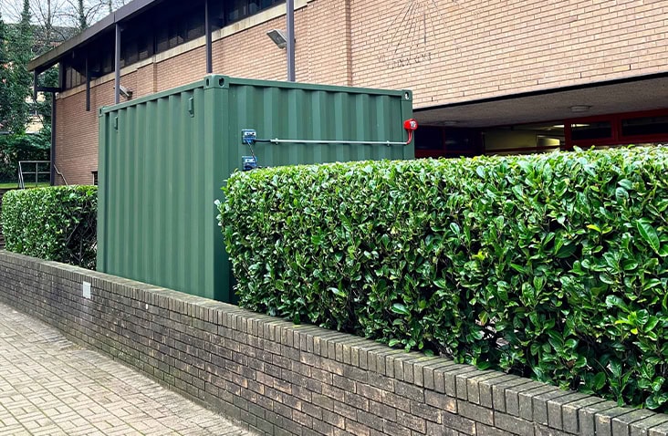 Green 10ft shipping container converted into a battery testing storage unit, featuring a secure personnel access door, reinforced steel locking bars and industrial-grade paint finish, designed for safe on-site battery testing and storage.  