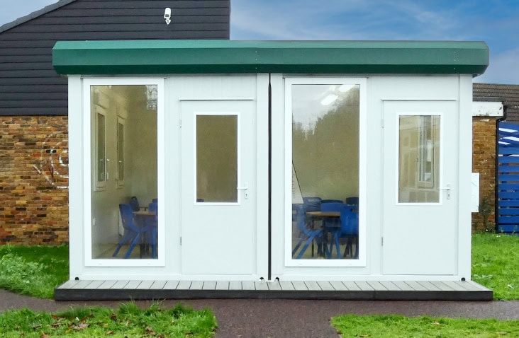 Modular classroom unit installed at Carrington School, showing a white bay modular building with glazed doors and window, internal classroom furniture visible through the glazing.
