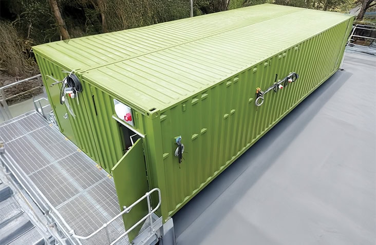 Two 40ft shipping containers combined to form a switchgear enclosure, showing a green containerised plant room with personnel access door, external cable connections, safety fixtures and integrated access walkway for electrical infrastructure installations.