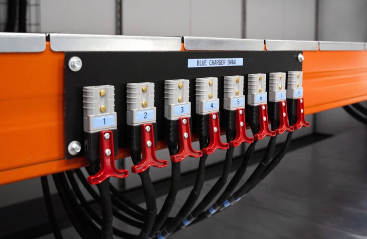 Close-up of industrial battery charger connections mounted on orange steel racking, showing numbered charging points inside a containerised battery charging container. 