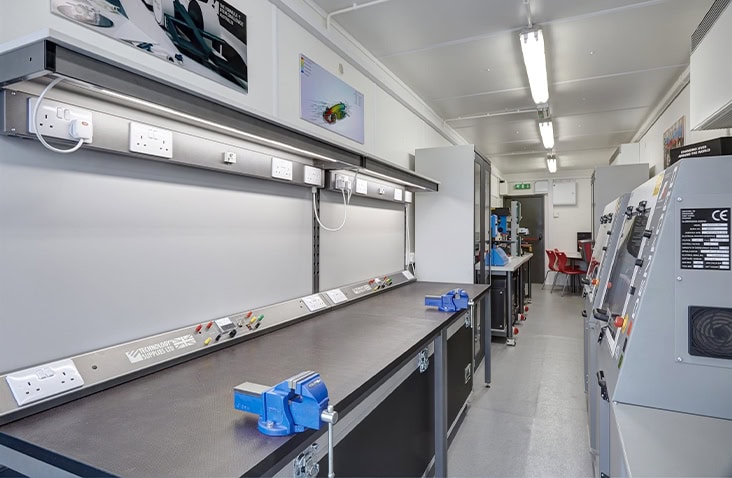 Interior of a containerised STEM workshop featuring fixed workbenches, electrical sockets, vices and industrial machinery, designed as a practical learning space for students inside a converted shipping container.