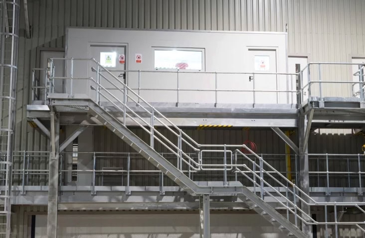 Elevated containerised control room conversion installed inside an industrial facility, featuring an external steel staircase, raised access platform and safety handrails, providing secure access to a control and monitoring space overlooking plant operations. 