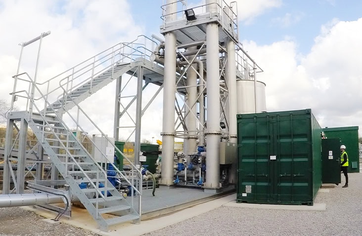 Containerised water treatment system installed on site for Evergreen Water Solutions, showing a green converted shipping container positioned alongside industrial pipework, access stairs and processing infrastructure at a treatment facility. 