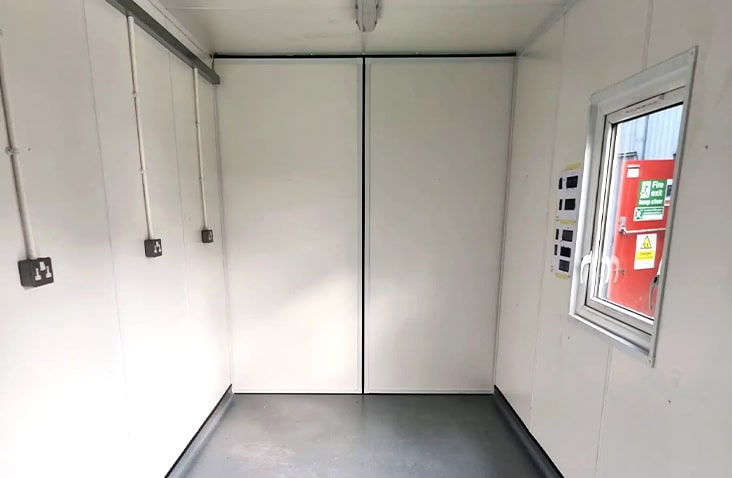 Interior of an NPK recovery workshop container, showing a clean, insulated shipping container interior with electrical sockets, wall panels, durable flooring and a window providing natural light. 