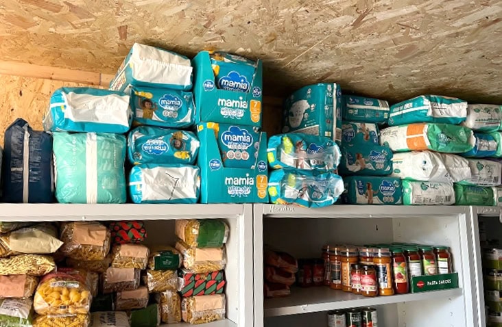 Shelving inside a shipping container food storage unit, stocked with nappies, baby supplies, tinned food and dry goods for community distribution. 