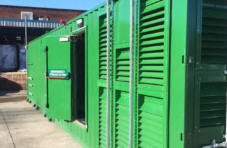 Green shipping container conversion with full-height acoustic louvres and emergency exit door, designed to house industrial plant and equipment with ventilation and noise control for on-site energy or power applications. 