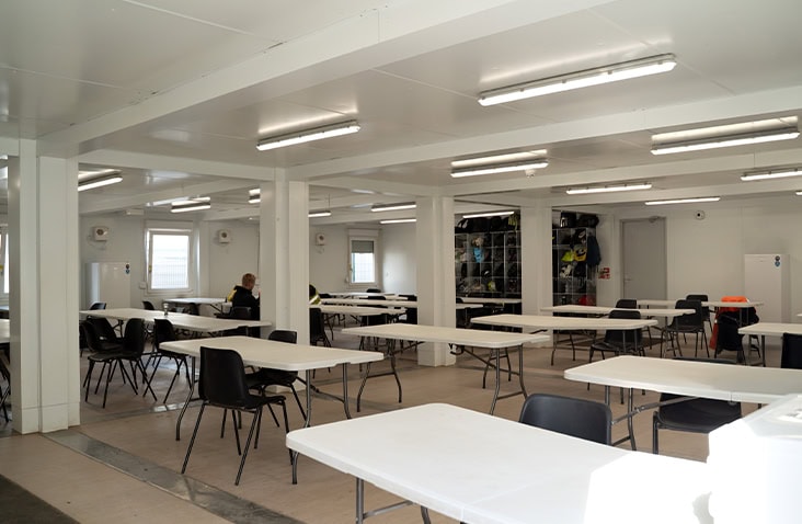 Interior of a large modular canteen building with rows of tables and chairs, bright LED lighting and open layout, designed for workforce welfare on construction and infrastructure sites. 