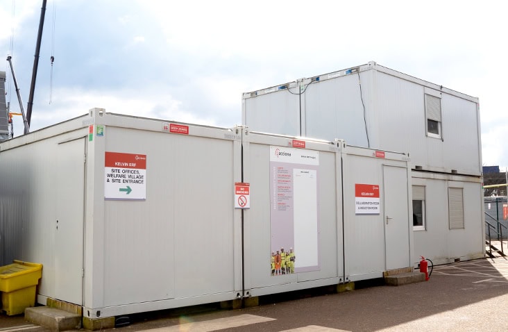 Modular welfare and office accommodation units installed on a construction site, showing ground-floor modular buildings with clear signage for site offices, welfare village and site entrance. 