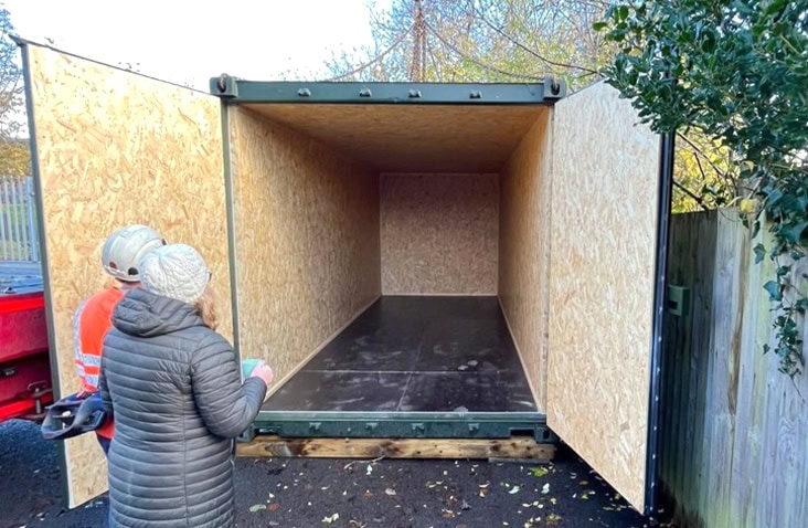 An empty shipping container lined with timber panels, shown during site positioning for use as a secure foodbank storage container. 