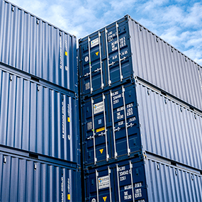 Rows of blue shipping containers stacked in a container yard, showing secure steel storage containers available for short-term and long-term hire. 