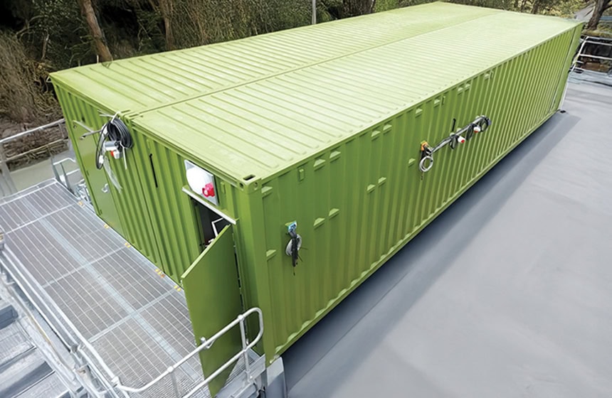 Two 40ft shipping containers combined to form a switchgear enclosure, showing a green containerised plant room with personnel access door, external cable connections, safety fixtures and integrated access walkway for electrical infrastructure installations.