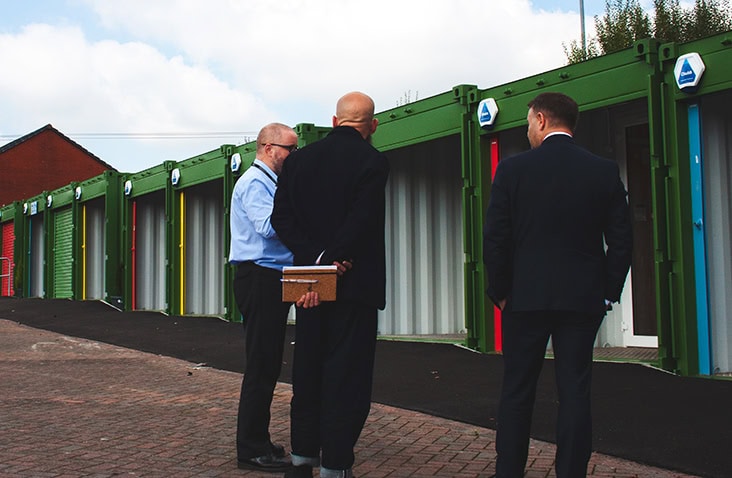 Staff and visitors outside container-based business units, showing people discussing units in front of converted shipping containers used for enterprise and commercial workspace. 