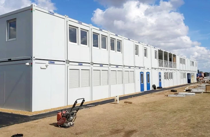 Modular school under construction on site, showing a multi-storey arrangement of white modular units with windows, doors and ventilation panels forming a temporary or permanent site accommodation complex.