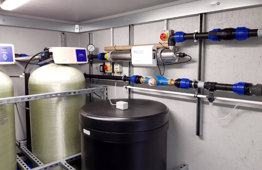 Interior of a containerised water treatment plant room showing filtration vessels, chemical dosing equipment, control units and fixed pipework installed within a specialist containerised utility enclosure. 